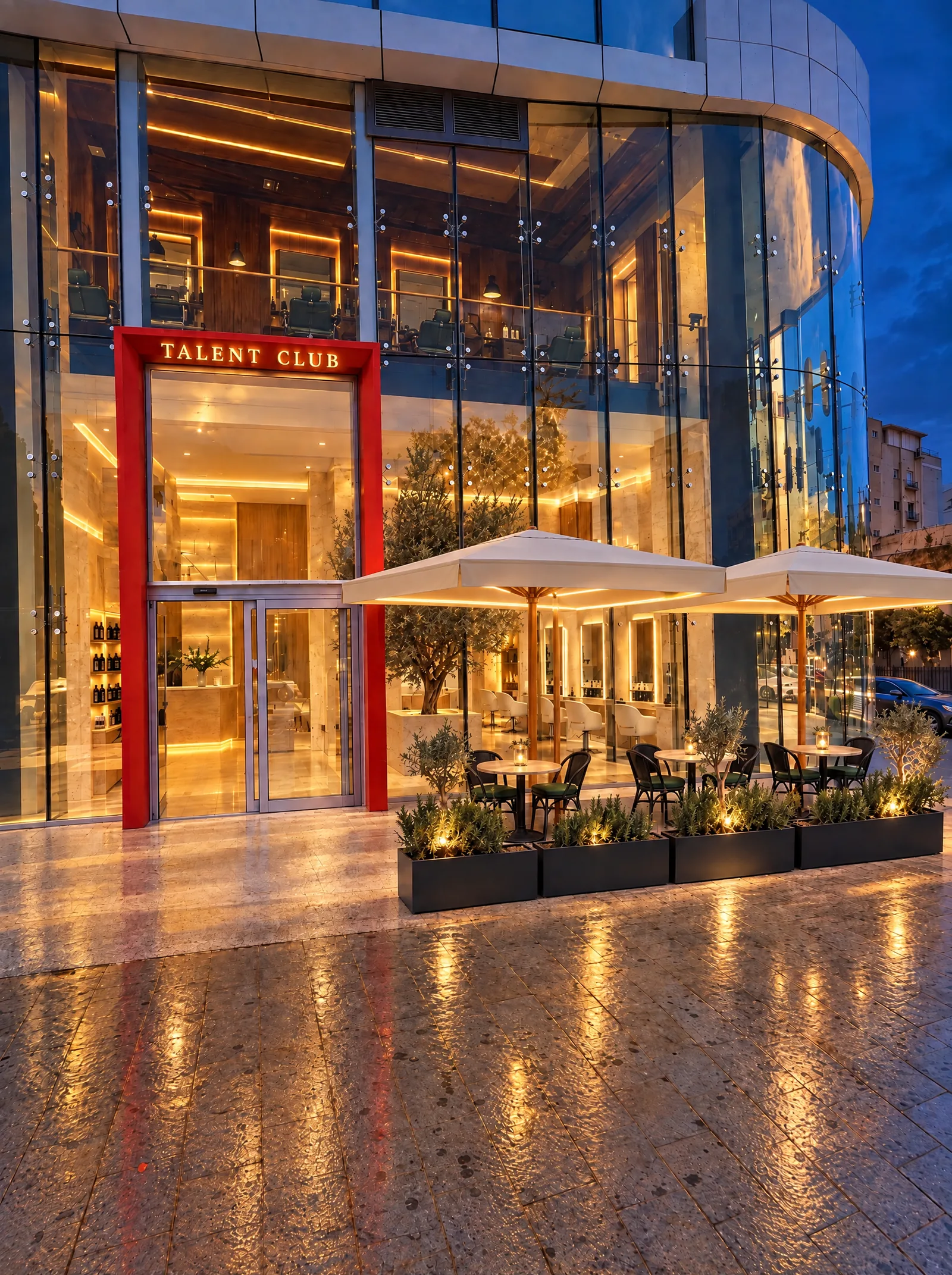 La façade vitrée illuminée, le portail rouge TALENT CLUB et la terrasse, le soir